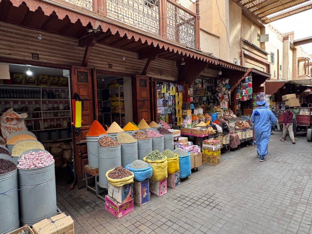 A street in the Marrakech souks lined with vibrant spice stalls showcasing colorful mounds of spices and herbs in a traditional market setting.