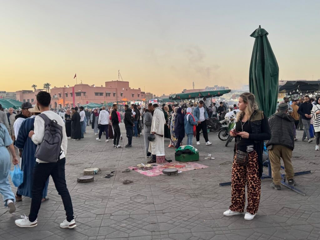 Jemaa el-Fnaa square in Marrakech at sunset, bustling with locals and tourists enjoying street performances, market stalls, and traditional Moroccan culture.