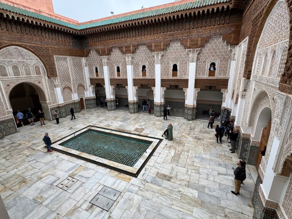 Courtyard of Medersa Ben Youssef in Marrakech, featuring a central water basin, intricate carvings, and stunning Moroccan tilework.