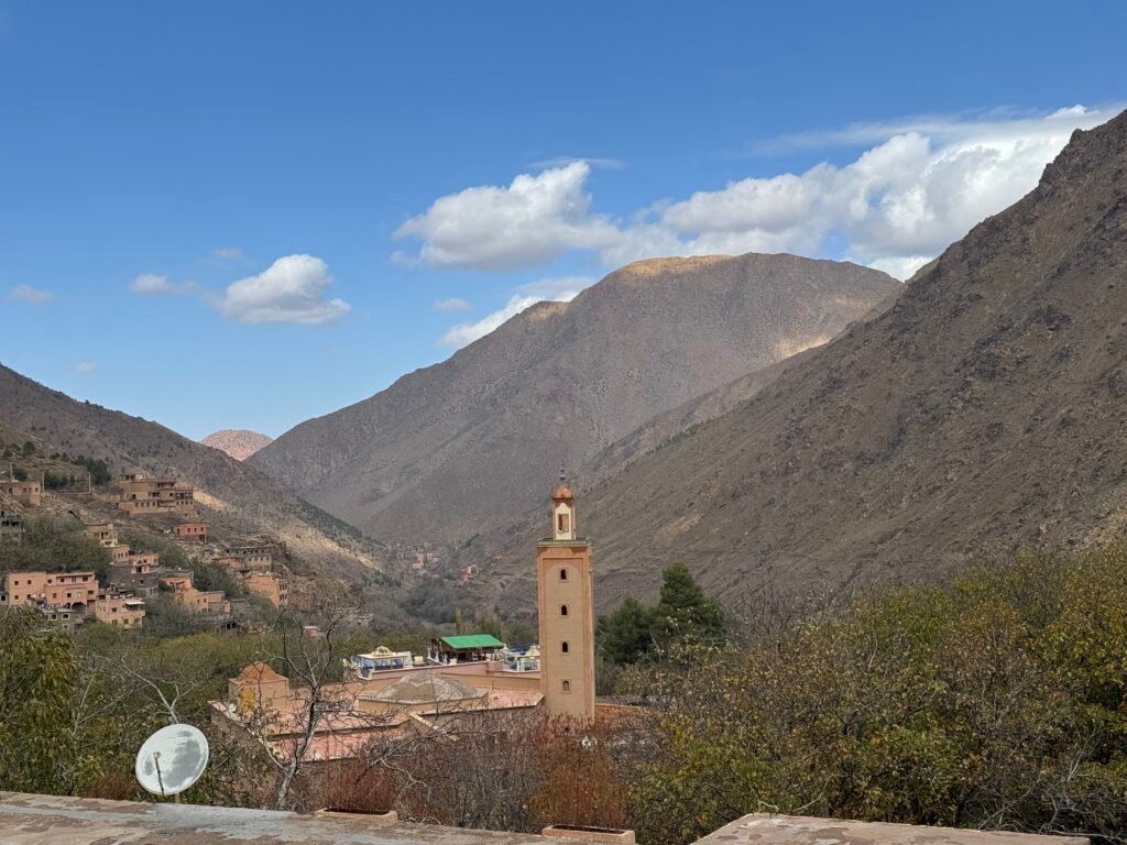 Scenic view of a Berber village nestled in the Atlas Mountains near Marrakech, featuring traditional architecture and a mosque surrounded by rugged mountain peaks.