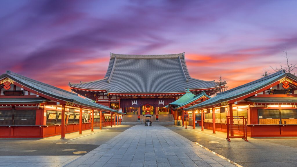 Senso-ji Temple in Tokyo, Japan, at dawn, with a vibrant sky casting a warm glow over the historic Buddhist temple. The illuminated pathways and traditional architecture create a serene and majestic atmosphere.