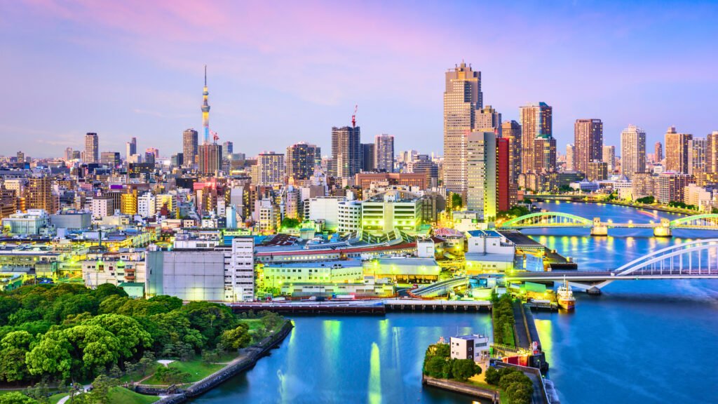 Stunning view of Tokyo’s skyline at dusk, featuring the Sumida River, illuminated bridges, and Tokyo Skytree towering above the cityscape, with vibrant city lights reflecting on the water.