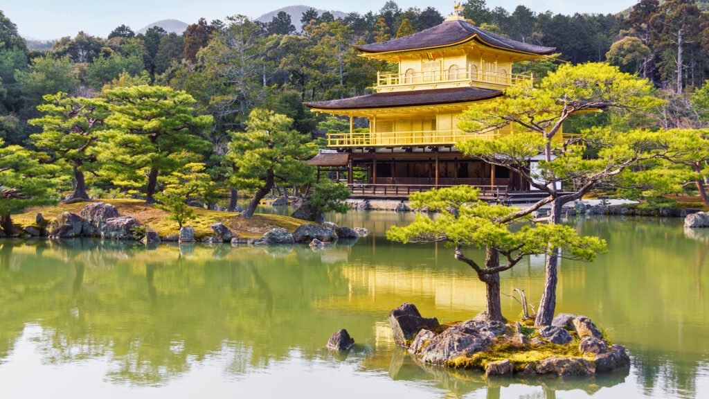 A stunning view of Kinkaku-ji, the Golden Pavilion, in Kyoto, Japan. The Zen Buddhist temple, covered in gold leaf, reflects beautifully on the surrounding pond, creating a serene and picturesque scene with lush greenery and distant mountains in the background.