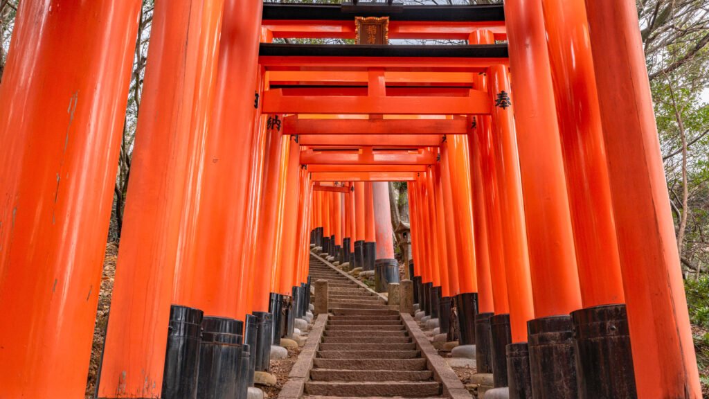 A mesmerizing view of the vermilion torii gates at Fushimi Inari Taisha in Kyoto, Japan. The iconic pathway, lined with thousands of bright red gates, leads up Mount Inari, creating a breathtaking and spiritual atmosphere at one of Kyoto’s most famous Shinto shrines.